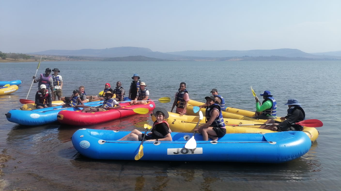School learners in life jackets and helmets paddling a raft together